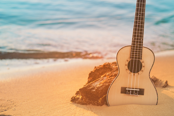 Guitar ukulele on sand beach with clear water and blue sky. Travel and lifestyle Concept.